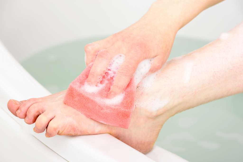 A bare foot being cleaned in the bath with a sponge
