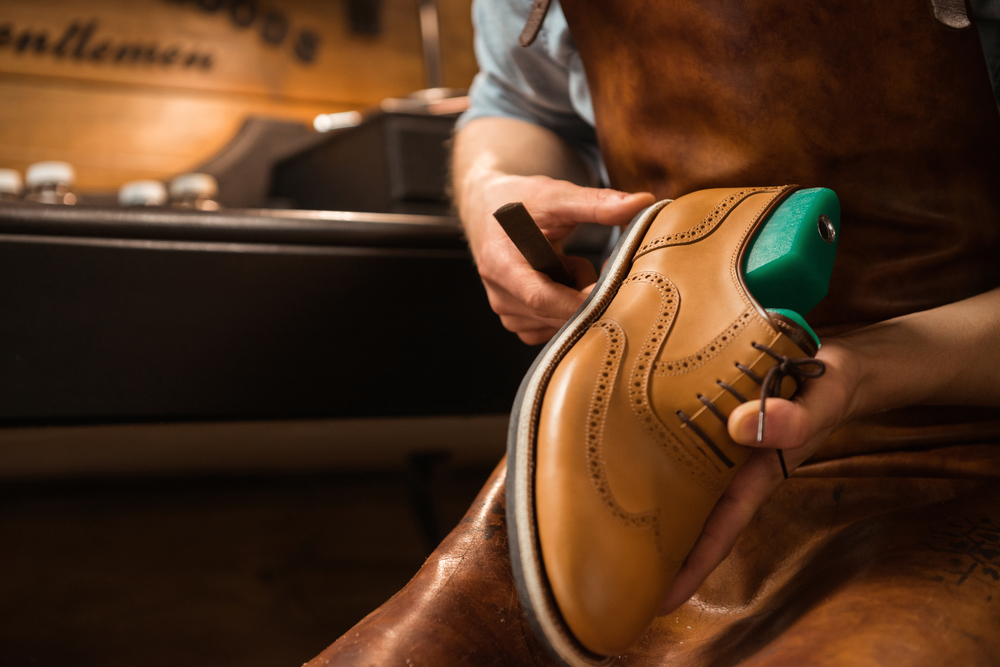 A cobbler holding a brown brogue shoe in a workshop.